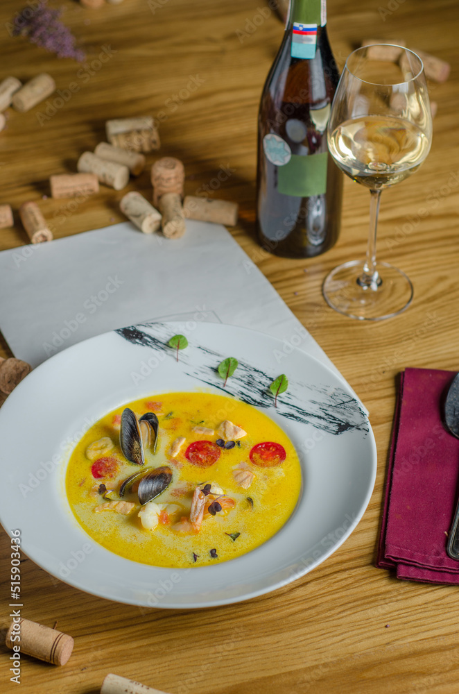 Soup with seafood - red fish, shrimps, mussels and tomatoes. The yellow soup is served with white wine. Dish in a restaurant.