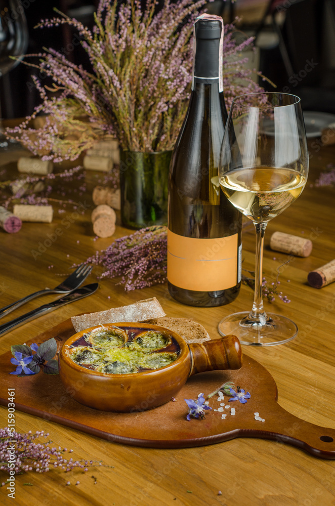 Burgundy snails with green butter and cheese, gourmet dish, in traditional ceramic pans with bread and glass of white wine on a wooden table