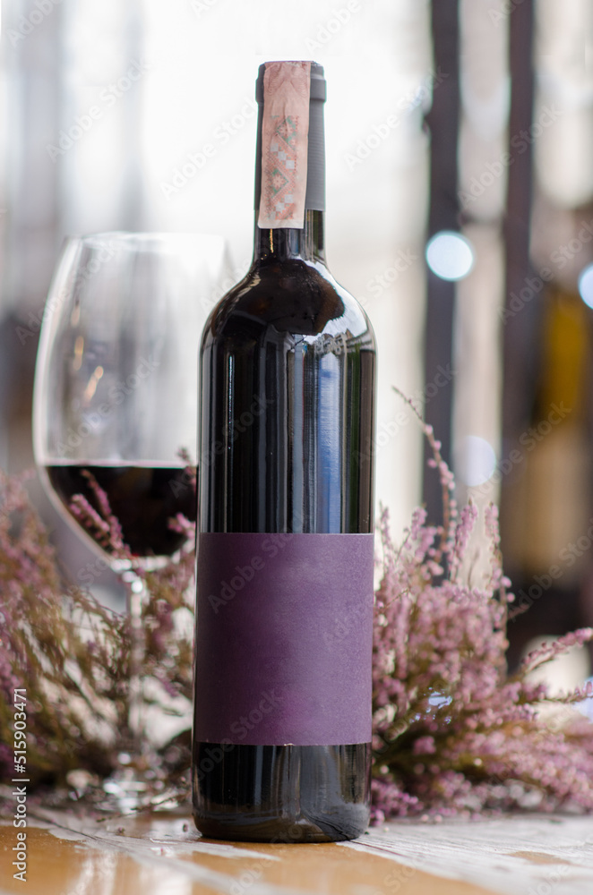 Fototapeta premium A bottle and a glass of red wine on a wooden table on a wine bar background. Bottle caps on the table. Place for text. Wine bar