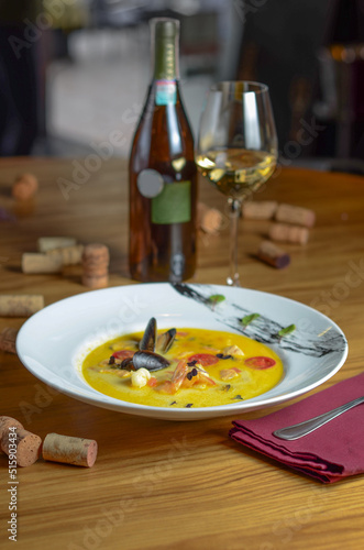 Soup with seafood - red fish, shrimps, mussels and tomatoes. The yellow soup is served with white wine. Dish in a restaurant.