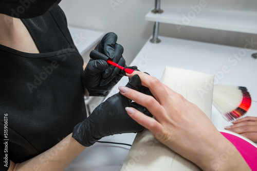 The manicurist paints the client s nails with red polish.