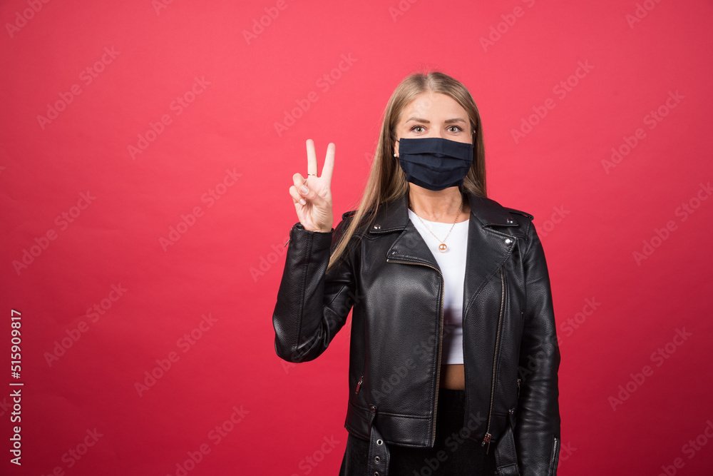 Beautiful young woman in a medical face mask showing victory sign Beautiful young woman in a medical face mask showing victory sign