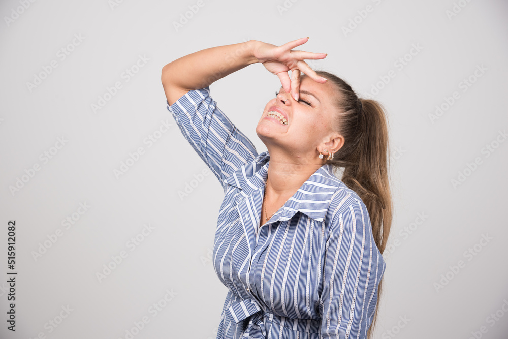 Young woman holding her nose on gray background Young woman holding her nose on gray background