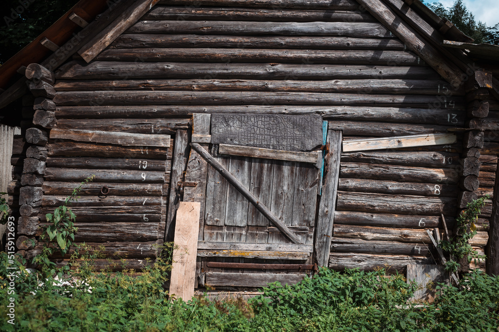 A beautiful log facade of a village house, rickety from old age. Green grass at the entrance.