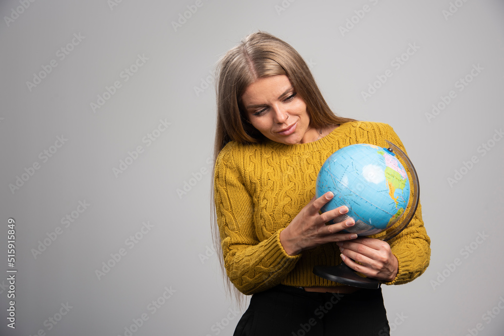 Blonde girl holding a globe and checking world map Blonde girl holding a globe and checking world map
