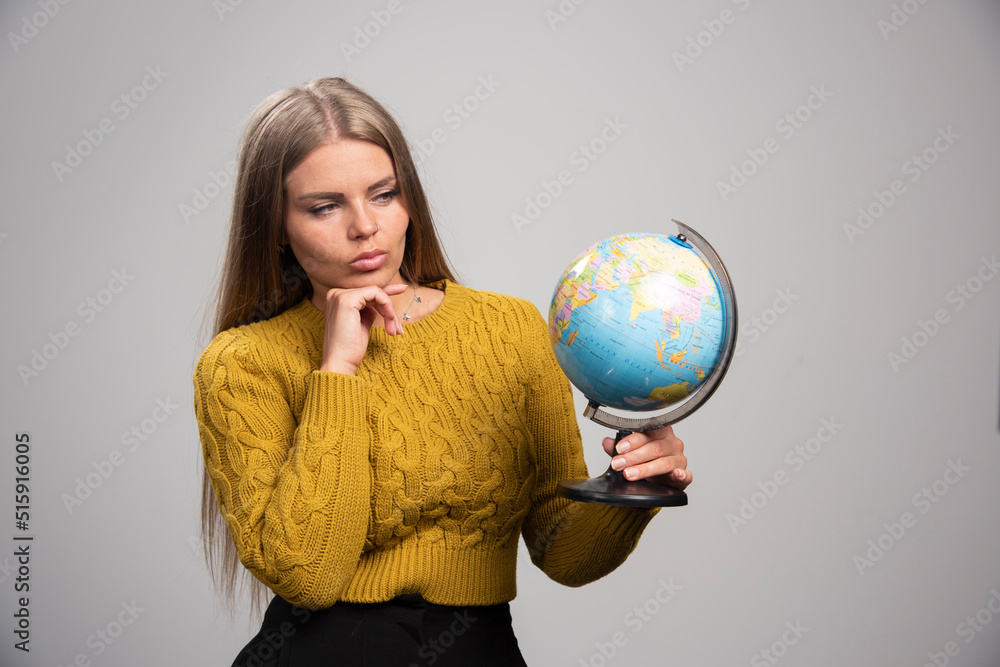 Blonde girl holding a globe and checking world map Blonde girl holding a globe and checking world map