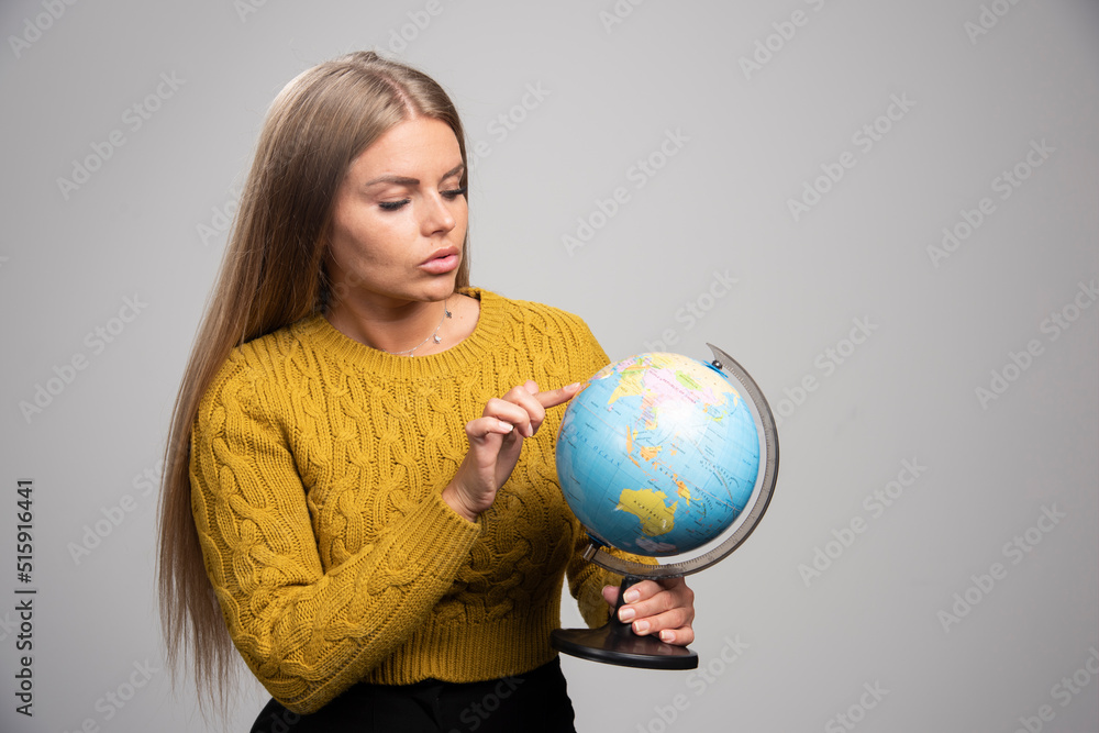 Blonde girl holding a globe, thinking and pointing the destinations over it Blonde girl holding a globe, thinking and pointing the destinations over it