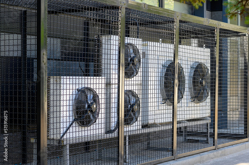 Air conditioning compressor system on a modern building protected by a metal fence.