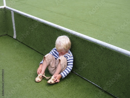 sad boy kid sitting on the lawn of the stadium