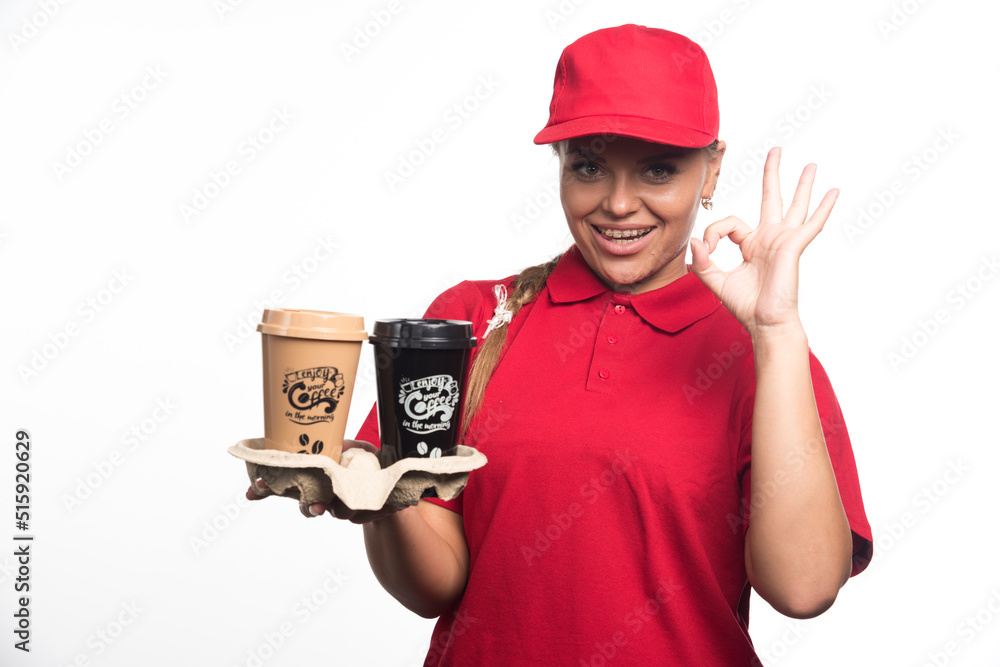 Woman with cap showing ok gesture and holding cups of coffee on white background Woman with cap showing ok gesture and holding cups of coffee on white background