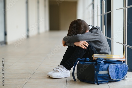Upset boy sitting at school and crying after bullying by pupils classmates. The child covered his face with his hands and cries. photo