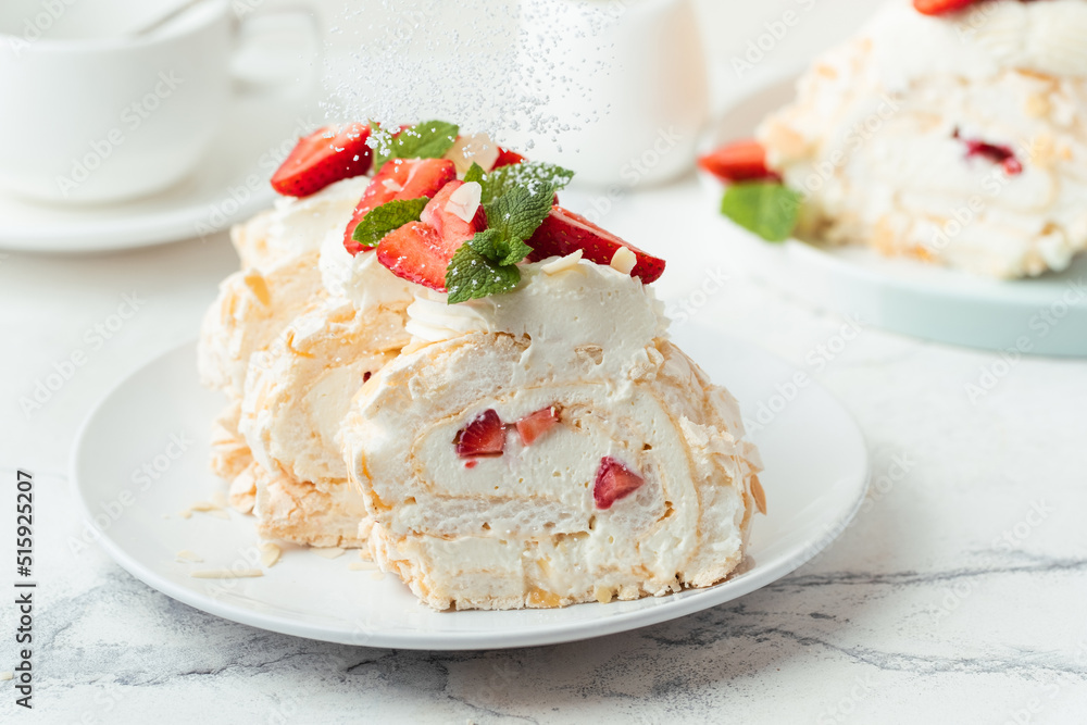 Meringue roll sprinkled with powdered sugar decorated with strawberries sliced and served in the white plate on the white background. Macro shot Meringue roll sprinkled with powdered sugar decorated with strawberries sliced and served in the white plate on the white background. Macro shot