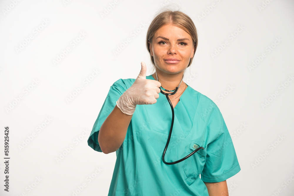 Blonde female doctor in blue uniform with stethoscope in the neck making thumb up sign Blonde female doctor in blue uniform with stethoscope in the neck making thumb up sign