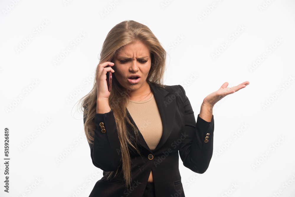 Young businesswoman in black suit looks angry while talking to phone Young businesswoman in black suit looks angry while talking to phone