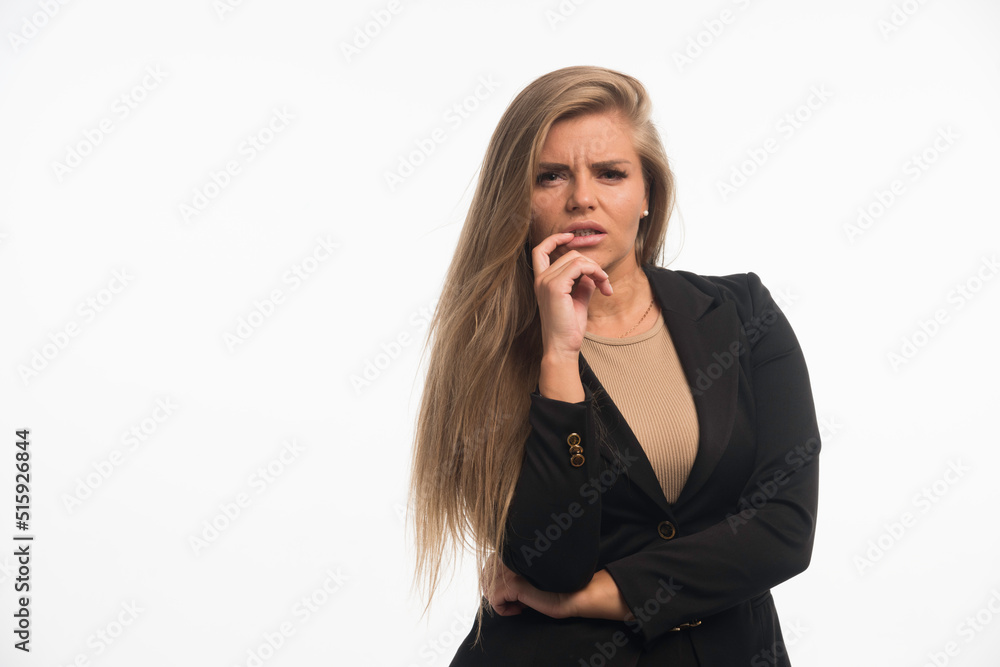 Young businesswoman in black suit looks confused with finger at her mouth Young businesswoman in black suit looks confused with finger at her mouth