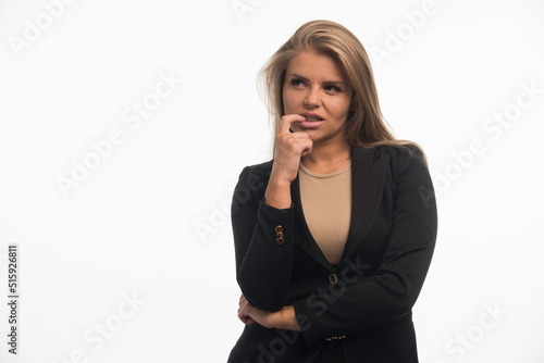 Young businesswoman in black suit looks confused with finger at her mouth
