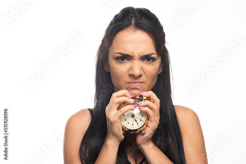 Angry young woman holding an alarm clock on white background