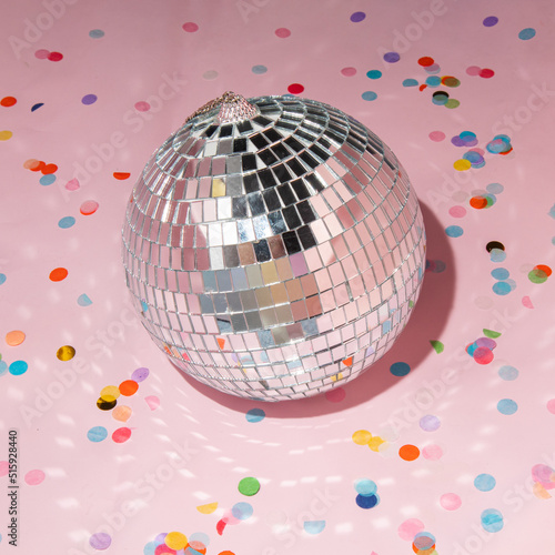 Shiny disco ball and colorful confetti on pastel light pink background. Trendy party symbols concept. Minimalistic celebration composition.