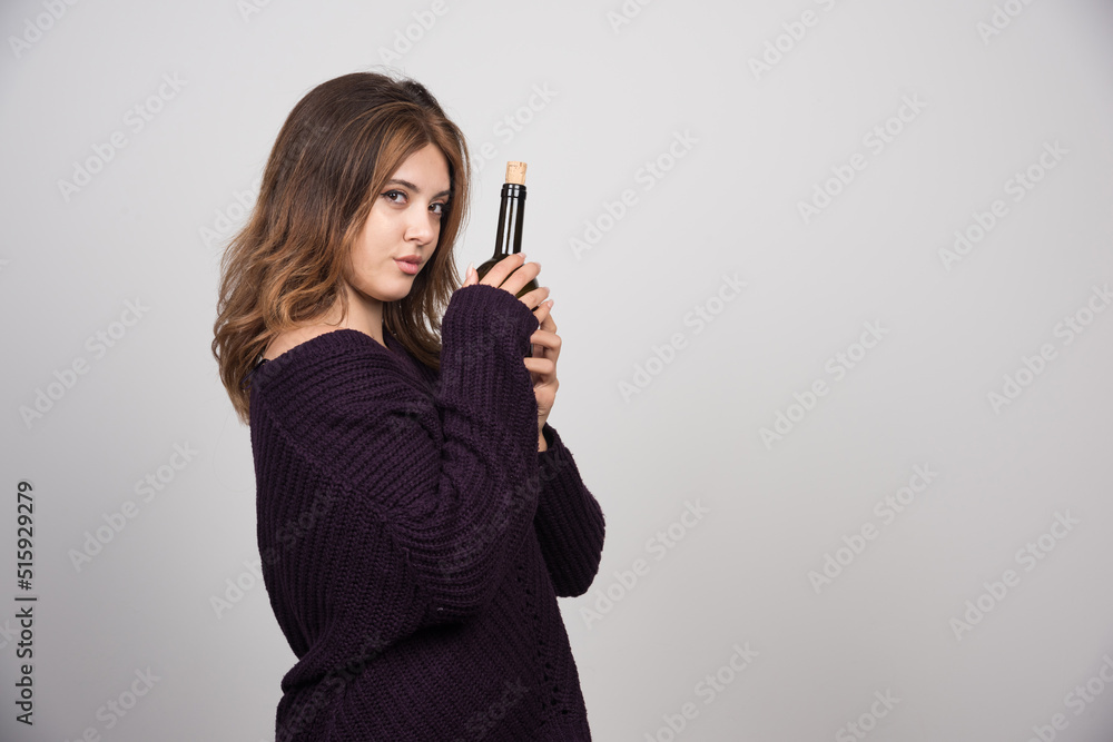Young woman in warm knitted sweater holding a bottle of wine Young woman in warm knitted sweater holding a bottle of wine