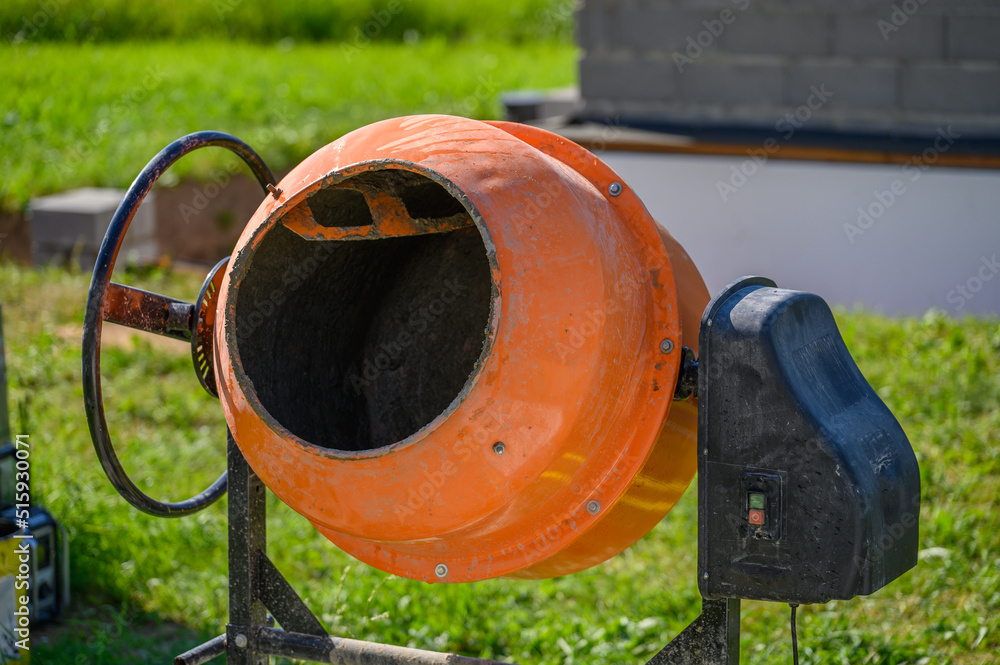 Concrete Mixers. Small. Orange. For home repairs. For doing simple jobs. Concrete is made with an electric concrete mixer, the photo was taken outdoors on a sunny summer day. Concrete Mixers. Small. Orange. For home repairs. For doing simple jobs. Concrete is made with an electric concrete mixer, the photo was taken outdoors on a sunny summer day.