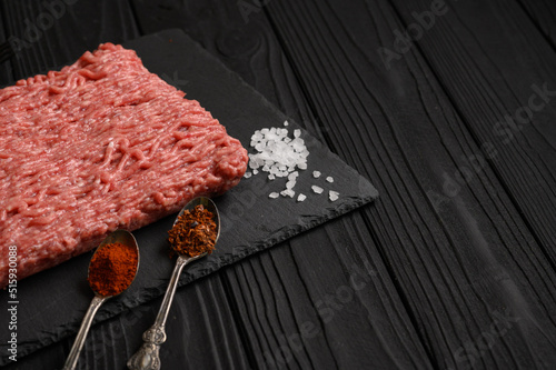 Fresh raw meat or ground chicken meat on a wooden cutting board with thyme, spices and garlic. Black wooden background. Top view. Copy space.
