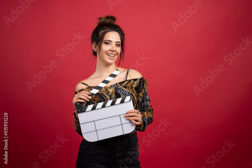 Brunette girl holding a blank clapper board for film production on red background