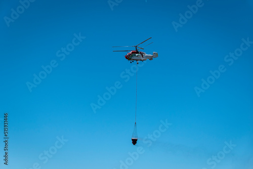 Helicóptero a voar enquanto transporta uma grande quantidade de água no seu balde em baixo para apagar um incêndio photo