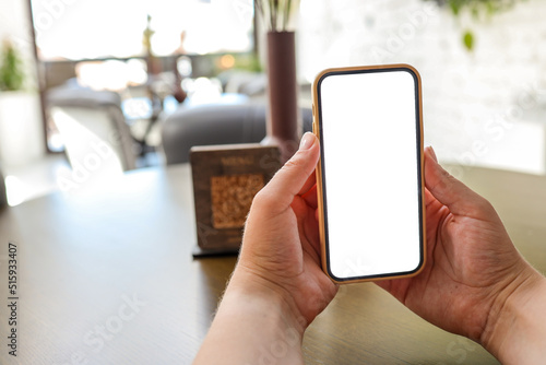 Mockup image of woman's hands holding white mobile phone with blank screen in cafe