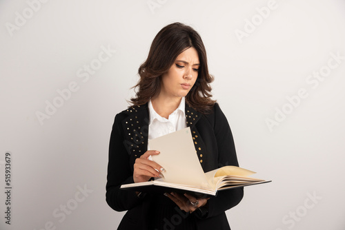 Young female teacher looking through notebook on white background