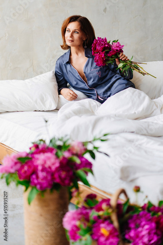 happy morning. a woman in pajamas in bed with a peonies. © andrey