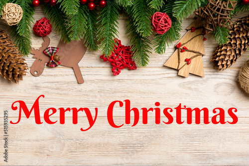 Merry Christmas text. Top view of Christmas toys, decorations and fir tree branches on wooden background. New Year holiday concept with copy space