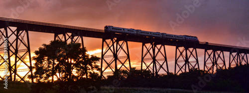 Slika na platnu Train crossing a bridge at sunset