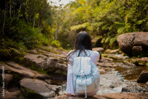 Mujer con una mochila sentada frente a un rio en la selva. Concepto de viajes y turismo photo