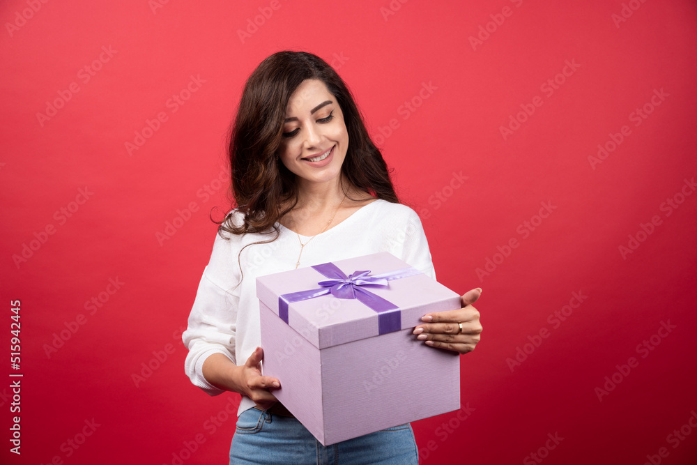 Young woman looking at purple present on red background