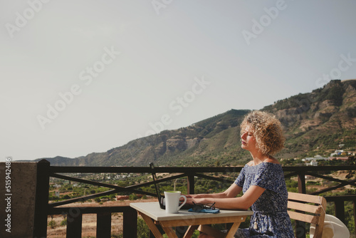 Relaxed woman works on her laptop on a terrace in the mountains.