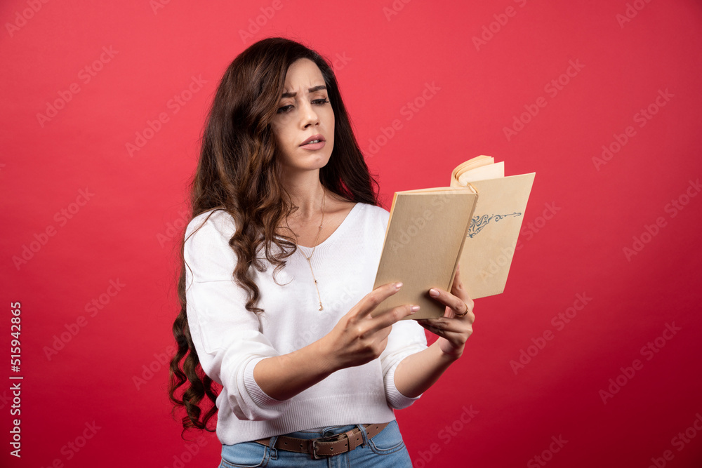 Young woman reading an interesting book on a red background Young woman reading an interesting book on a red background