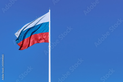 Waving Russian flag against a blue sky and empty space for text. Room for text. National flag of the Russian Federation. Silky shiny texture.