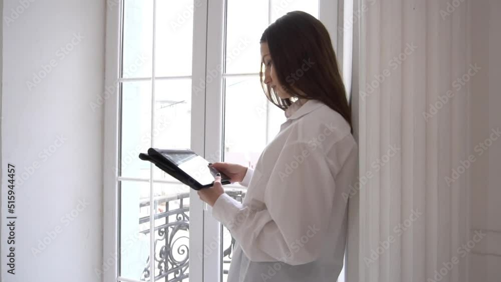 Slow Motion Woman browsing on a digital tablet while standing next to a window Slow Motion Woman browsing on a digital tablet while standing next to a window