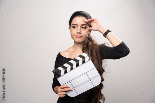 A filmmaker girl holding an open clapper board and looking confused or overthinking photo