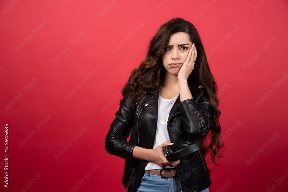Young woman holding headphones and posing on a red background Young woman holding headphones and posing on a red background