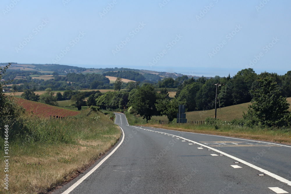 Downhill on an empty road in Somerset, England. Lush green rolling hills can be seen in the background Downhill on an empty road in Somerset, England. Lush green rolling hills can be seen in the background