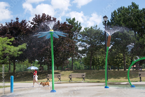 Woman walking the dog on a hot summer day in a spray park