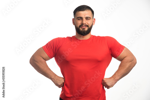Sportive man in red shirt demonstrating his arm muscles and looks confident © azerbaijan-stockers