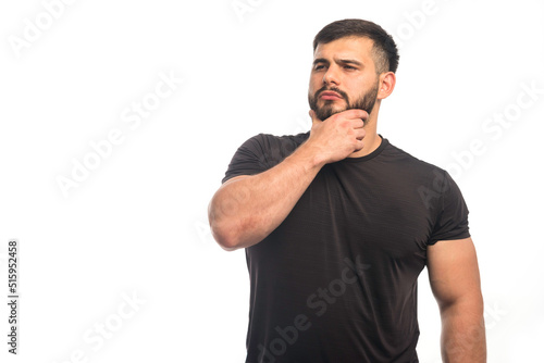 Sportive man in black shirt putting his hand to his beard