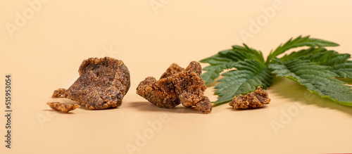 brown pieces of hashish and green cannabis leaf on a yellow background. photo