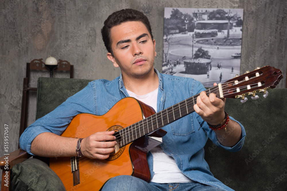 Obraz premium Young musician playing the guitar and sitting on sofa