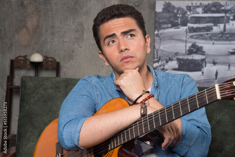 Obraz premium Young musician holding a beautiful guitar and sitting on sofa