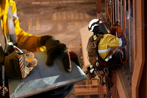 Construction miner supervisor wearing safety glove signing working at height working permit on open field job site prior to starting high risk rope access working at height construction mine site
