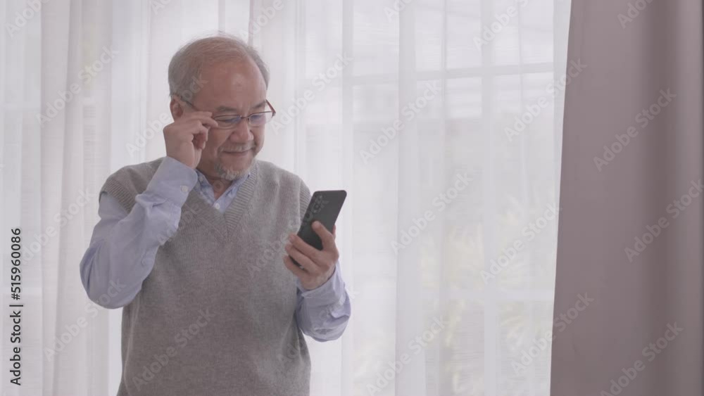 Elderly Asian man standing and play smartphone in living room with relaxing day. Elderly Asian man standing and play smartphone in living room with relaxing day.