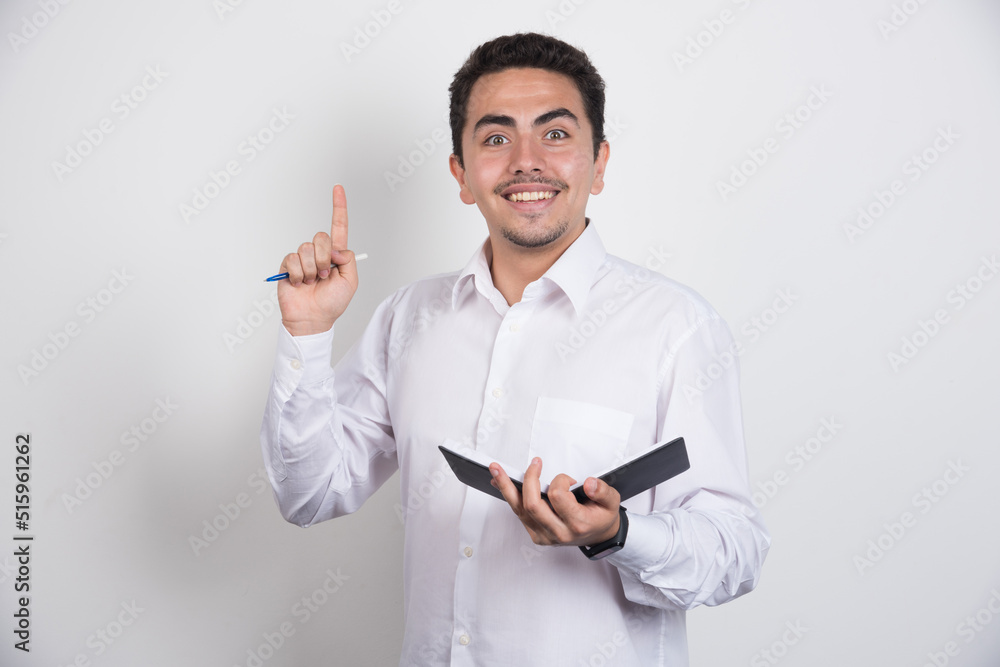 Positive businessman with notebook and pen pointing up on white background Positive businessman with notebook and pen pointing up on white background